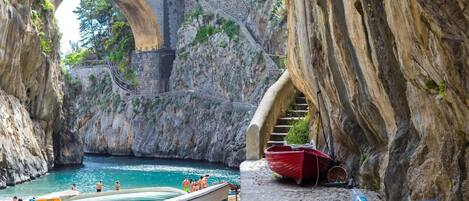 A stone bridge arching over a rocky shoreline with boats docked nearby.