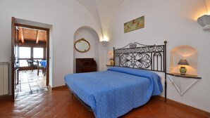 A bedroom with a bed, a nightstand, a wall-mounted lamp, a mirror, and a door leading to another room.