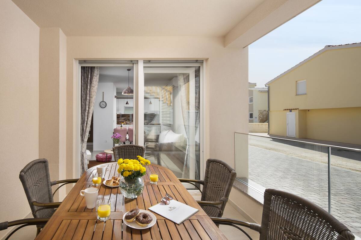 A balcony with a wooden table, wicker chairs, and a view of the street.