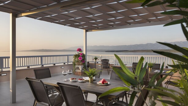 An outdoor patio with a table set for dining, chairs, and a view of the sea. - Apartments Vista Exclusive  (Vir)