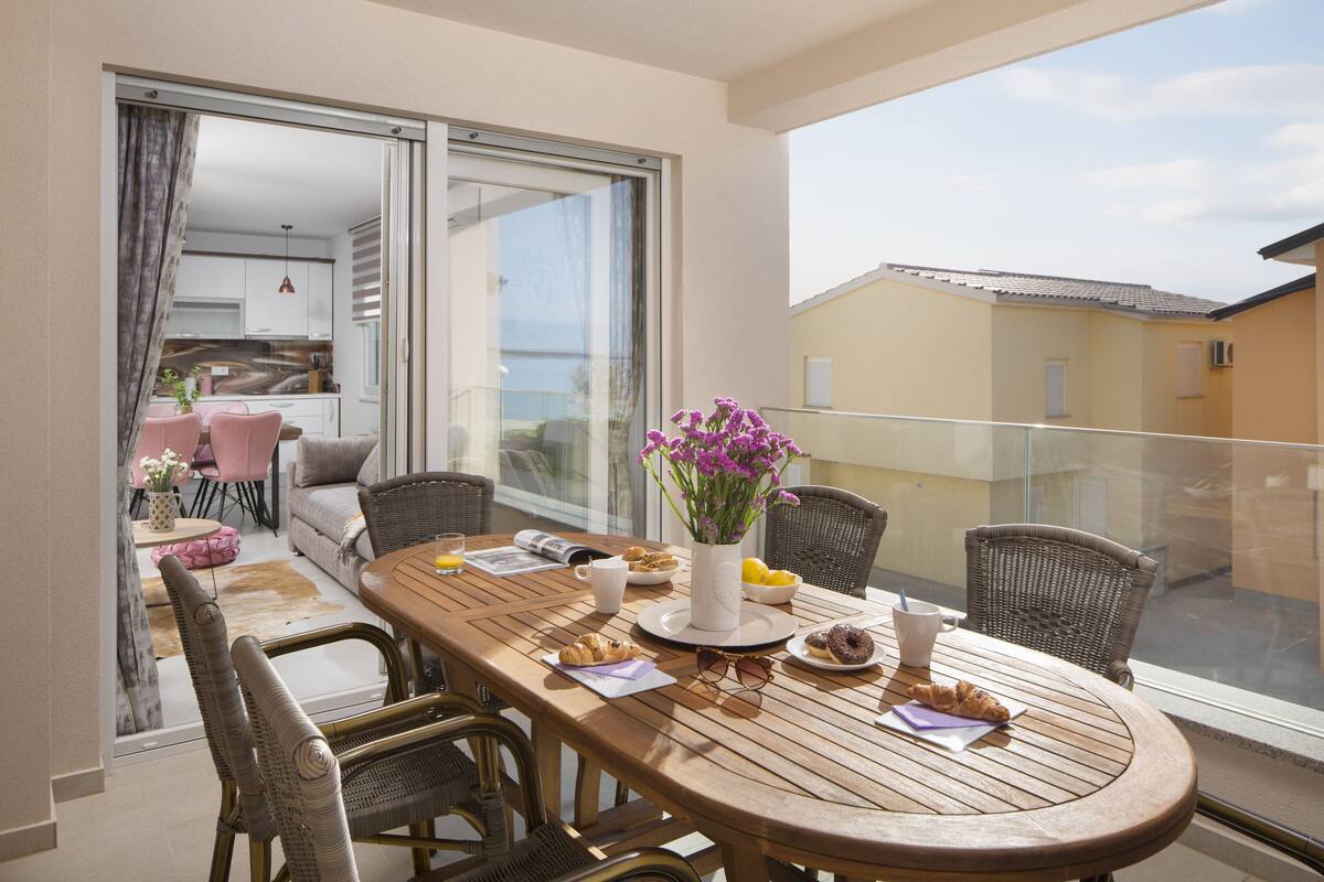 A balcony with a wooden table, wicker chairs, and a vase of flowers.