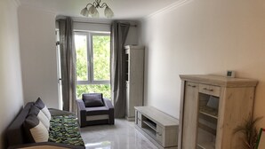 Ein modernes Wohnzimmer mit einer Couch, einem Sessel, einem Schrank und einem Fenster mit Vorhängen.