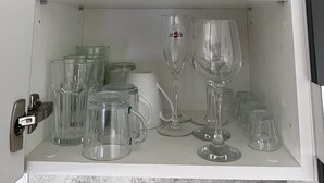 Ein Küchenschrank mit weißen Regalen, der Teller, Schüsseln und verschiedenes Glasgeschirr beherbergt.