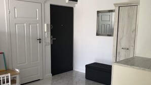 Ein Zimmer mit einer weißen Tür, einer schwarzen Tür, einem kleinen Tisch mit Stuhl, einer Bank und einem Schrank.