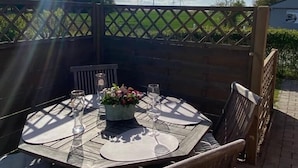 Un patio al aire libre con una mesa redonda dispuesta para comer, rodeado de sillas de madera.