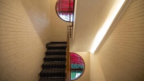 A staircase with patterned steps, two round windows with red frames, and a light fixture above. - Gemelli Hotel (Rome)