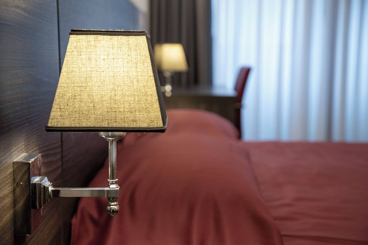 A hotel room with a bed, a nightstand, and a lamp.