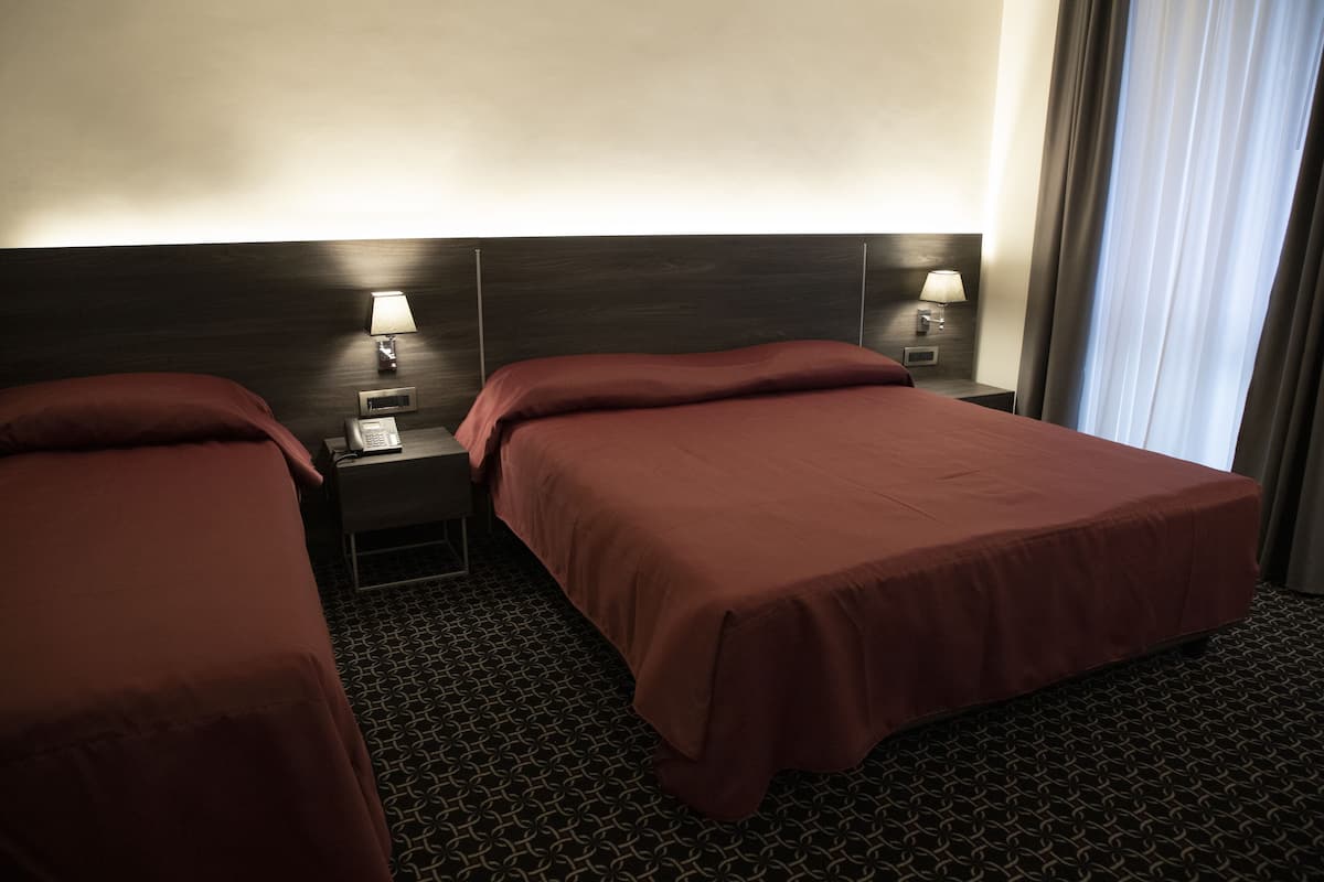 A hotel room with two beds, each with a headboard, bedside lamps, and a telephone on the nightstand.