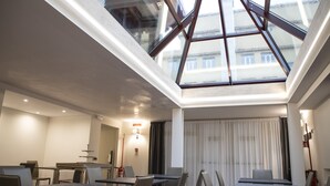 A hotel room with a skylight, a dining area with tables and chairs, and a view of buildings outside. - Gemelli Hotel (Rome)