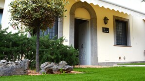 A building with a yellow facade, an arched doorway, and a small tree in the foreground. - Gemelli Hotel (Rome)