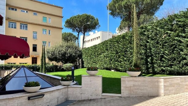 A courtyard with a paved area, a small pool with a red canopy, and a building with multiple windows in the background. - Gemelli Hotel (Rome)