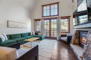 A living room with a green sofa, a fireplace, and large windows.