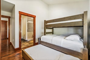 Una cama litera con ropa de cama blanca en una habitación con suelo de madera y una puerta de madera.
