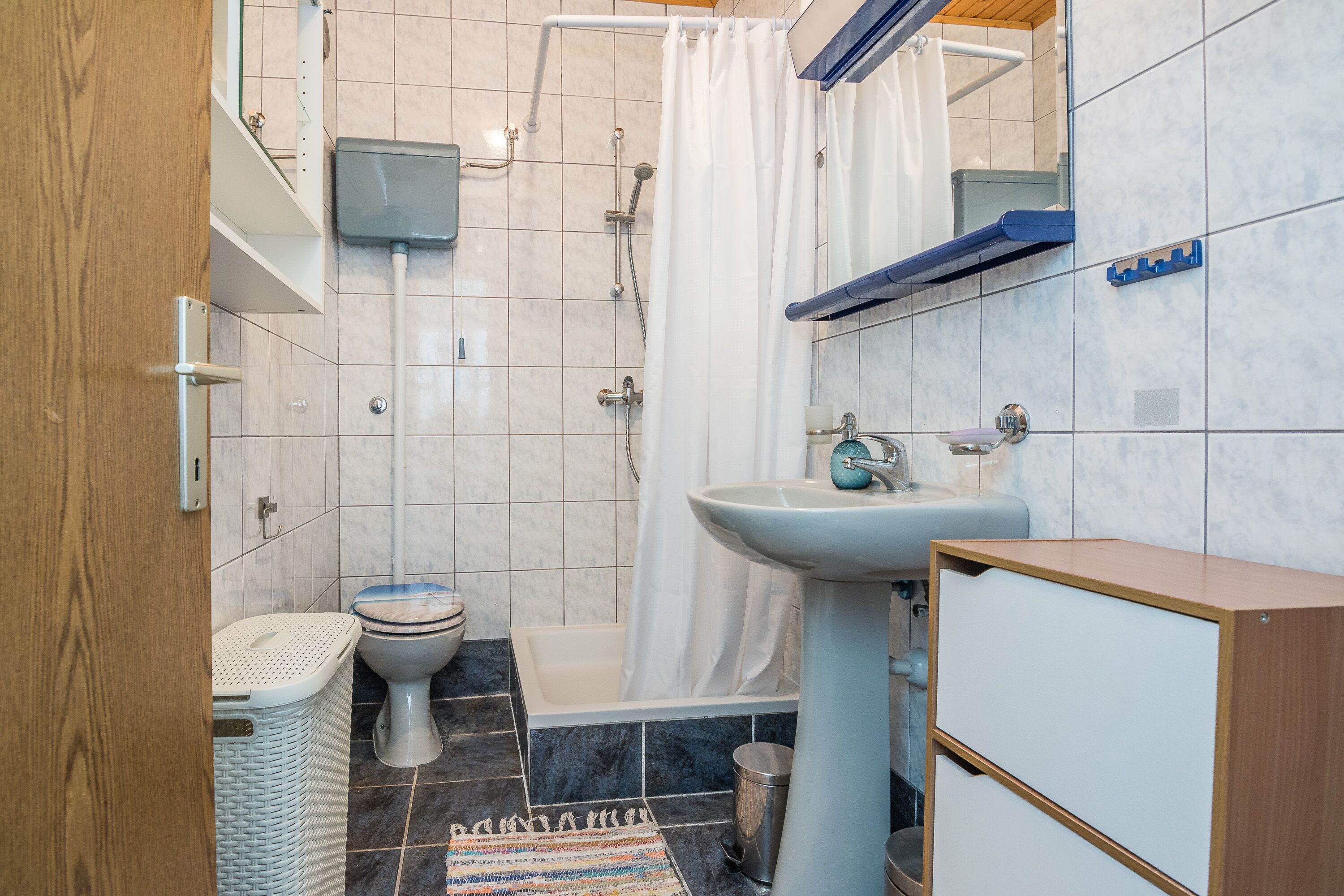 A bathroom with a toilet, sink, shower, and a small trash bin.