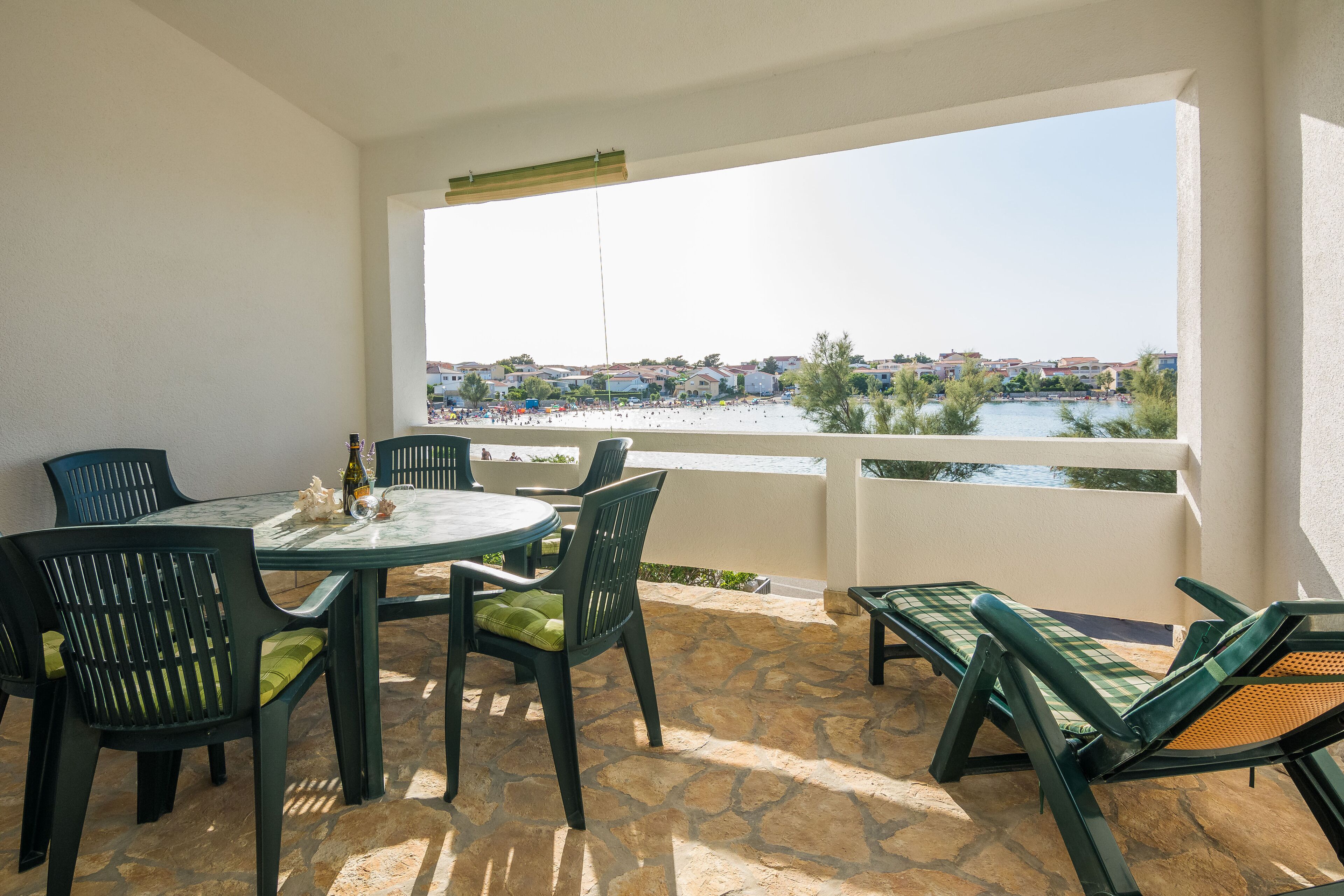 A balcony with a table and chairs, a view of a body of water, and a distant town.