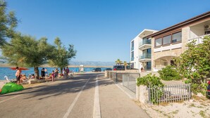 A coastal street with a building featuring balconies and a clear view of the sea. - Apartment Nada (Vir)