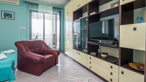 A living room with a leather sofa, a television on a wooden cabinet, and a large window with curtains. - Apartment Nada (Vir)
