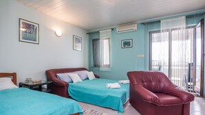 A hotel room with two beds, a red leather chair, and a view of the city through large windows. - Apartment Nada (Vir)