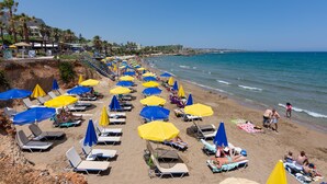 A beach with rows of sun loungers and umbrellas, a clear sky, and a calm sea. - Cretan Seaside Boutique Hotel (Hersonissos)