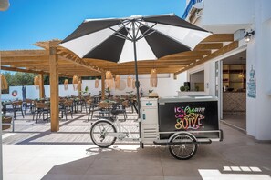 An outdoor seating area with tables and chairs, a bicycle, and an ice cream cart. - Cretan Seaside Boutique Hotel (Hersonissos)