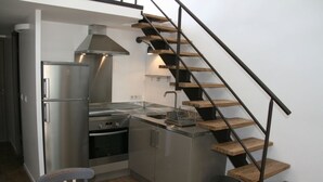 A compact kitchen with a built-in oven, a stainless steel refrigerator, and a wooden staircase.