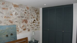 A room with a stone wall, a painting, a wooden bench, a small table with a lamp, and a large dark closet.