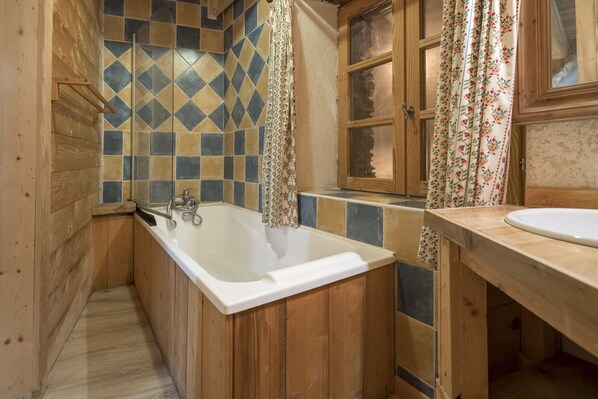 Un baño de madera con bañera, lavamanos y zona de ducha.