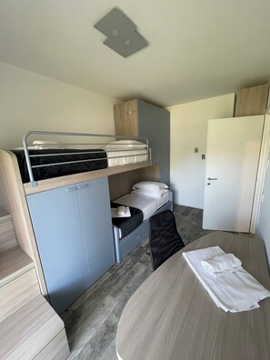 A compact, modern room with a bunk bed, a small desk, and a wardrobe.