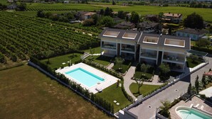 Un edificio moderno de varios pisos con piscina, rodeado de campos verdes exuberantes y viñedos.