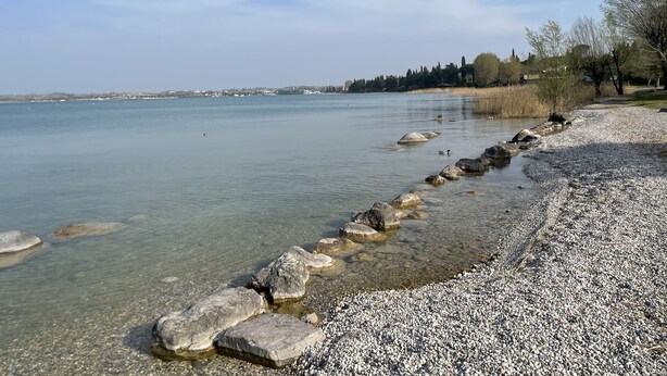 Una playa de guijarros con agua cristalina y una hilera de rocas que conducen a la orilla.