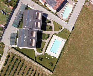 An aerial view of a modern residential property with a swimming pool, solar panels, and a well-maintained lawn.