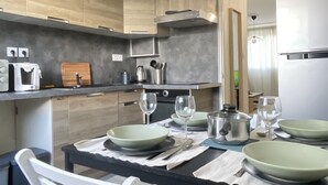 A modern kitchen with wooden cabinets, a stainless steel refrigerator, and a dining table set with plates and glasses. - Bright, open-plan apartment (Montauban)