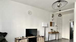 A modern living room with a flat-screen TV, wooden cabinets, a coffee table, and a dining area with a small table and chairs. - Bright, open-plan apartment (Montauban)