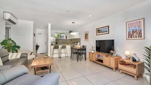 Una sala moderna con sofá, mesa de comedor, televisor y mesitas de madera.