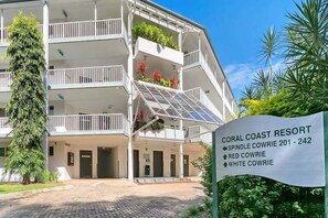 Un edificio a più piani con balconi, una targa con la scritta 'CORAL COAST RESORT' e un'area d'ingresso pavimentata.