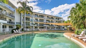 Un hotel con piscina, tumbonas y palmeras.