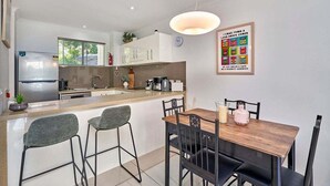 Una cocina moderna con comedor, refrigerador, cafetera y un reloj en la pared.