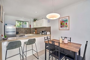 A modern kitchen with a dining area, a refrigerator, a coffee machine, and a clock on the wall.