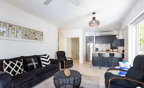 A modern living room with a black sofa, a round coffee table, and a dining area with bar stools.