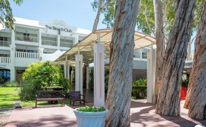 L'ingresso di un hotel con un portico coperto, alberi alti e un cartello che riporta "The Beach Club".