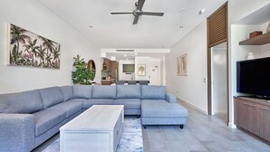 Un salon moderne avec un canapé d’angle, une table basse, un téléviseur et un ventilateur de plafond.