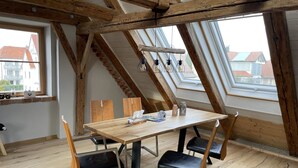 A room with a wooden table and four chairs, a skylight, and a view of buildings outside. - Lovingly restored vacation apartment in alpine chic style DG (Ottobeuren)