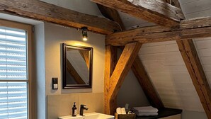 A modern bathroom with a wooden ceiling, a large mirror, a sink, and a window with blinds. - Lovingly restored vacation apartment in alpine chic style DG (Ottobeuren)