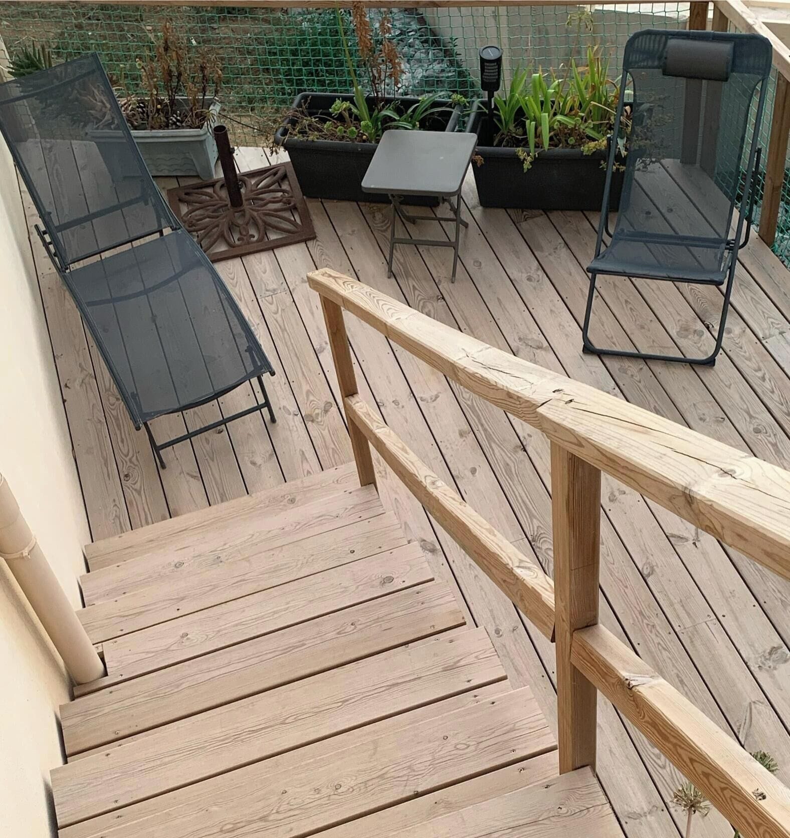 A wooden deck with a staircase, outdoor furniture, and planters.