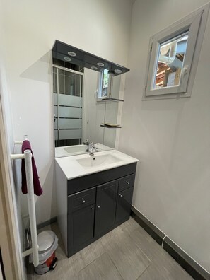 Ein Badezimmer mit einem weißen Waschbecken, dunklen Schränken, einem Spiegel und einem Fenster.