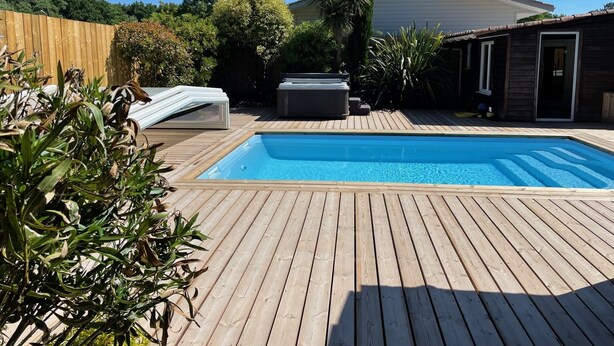 Una piscina con cubierta de madera, rodeada de follaje y una valla de madera.