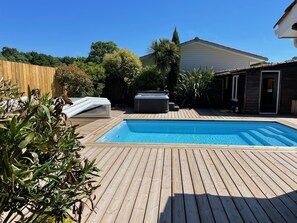 Ein Schwimmbad mit Holzterrasse, umgeben von Grünpflanzen und einem Holzzaun.