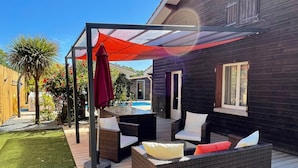 Un patio con mobiliario de mimbre, una mesa de vidrio y un paraguas rojo.