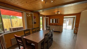 Un comedor con una mesa y sillas de madera, una cocina con armarios y un ventanal, y vista a una cerca de madera en el exterior.