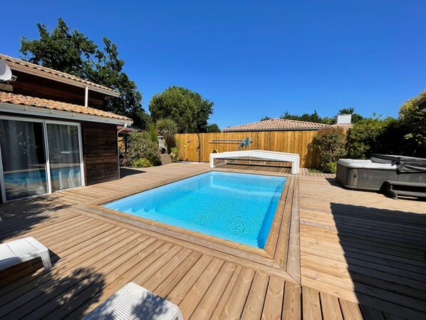 Eine Holzterrasse mit einem rechteckigen Swimmingpool, einem Whirlpool und einer überdachten Sitzgelegenheit.
